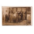 Grup de persoane în fața unei prăvălii, fotografie format carte poștală